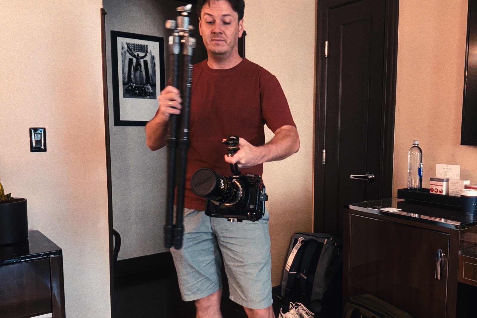 George V.K. in a New York hotel room holding a cinema camera rig and a folded tripod